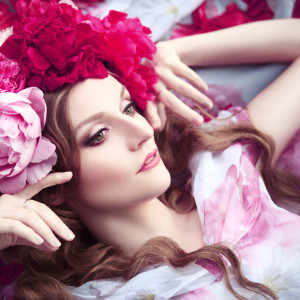woman in a wreath of peonies lies among petals