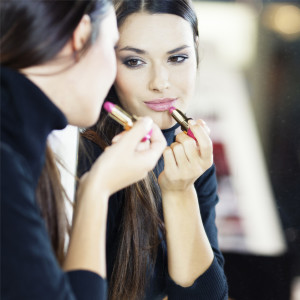 young woman applying lipstick in front of mirror